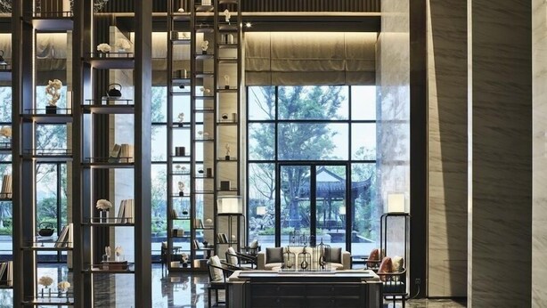 Un intérieur moderne avec un espace salon central, une grande étagère contenant divers objets et de grandes fenêtres offrant une vue sur l’extérieur.