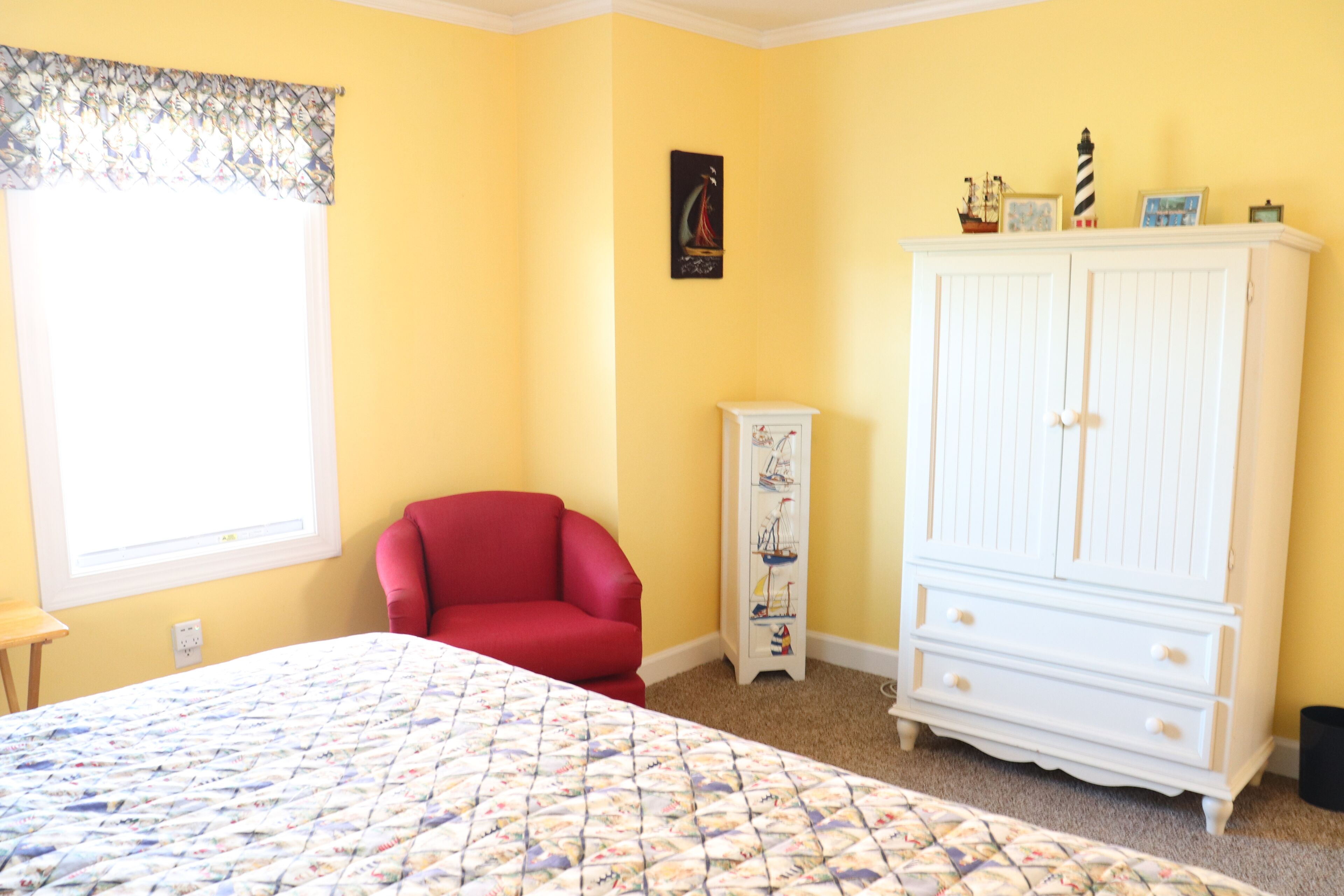 A bedroom with a bed, a red chair, a white dresser, and a window with a curtain.