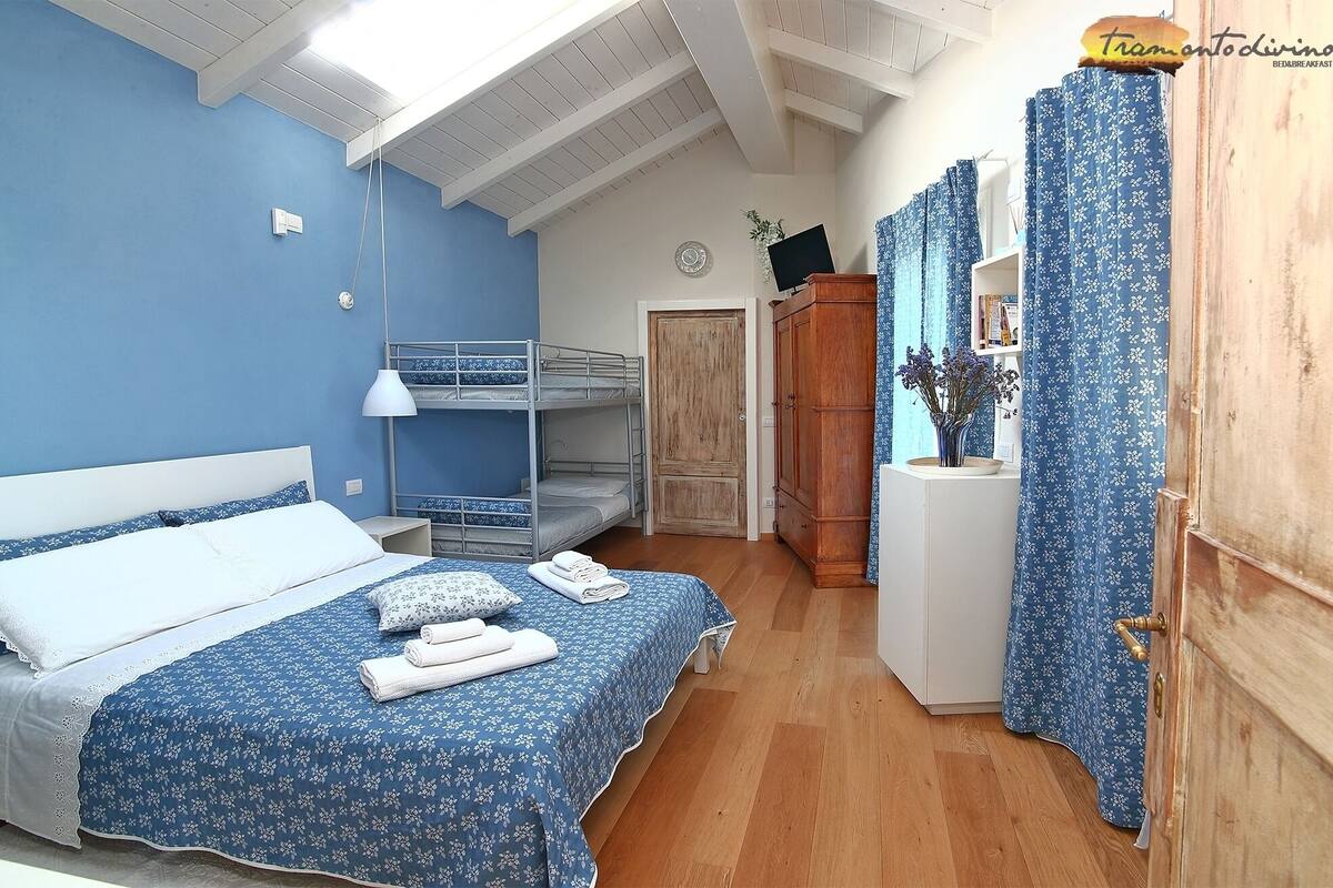 A bedroom with bunk beds, a wooden wardrobe, a desk with a vase, and a blue floral curtain.