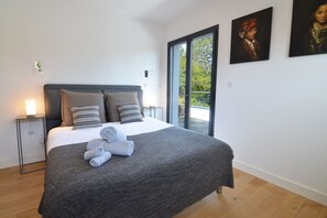 Ein modernes Schlafzimmer mit einem großen Bett, einem Nachttisch, einer Nachttischlampe und Blick durch eine Glastür.