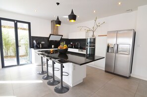 A modern kitchen with a central island, bar stools, a stainless steel refrigerator, and pendant lighting.