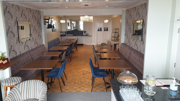 Een restaurant met ruimtes met zitbanken en tafels, een koffieapparaat en een toonbank met etalage.