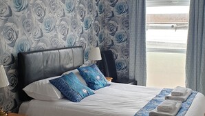 Een hotelkamer met een groot bed, een nachtkastje, een lamp, een stoel en uitzicht op buiten.