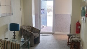 Een hotel lobby met gestreepte banken, een glazen salontafel, een blauwe lamp, een brandblusser en een deur naar buiten.