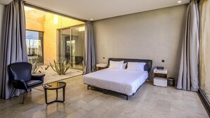 A modern bedroom with a large bed, a glass door leading to a balcony, a small table, and a chair. - Villa Amara Oliver Palm Resort (Marrakech)