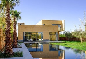 A modern house with a swimming pool, large windows, and a well-maintained lawn. - Villa Amara Oliver Palm Resort (Marrakech)