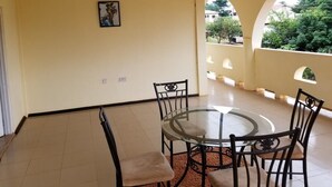 A dining area with a round glass table and black chairs, a ceiling fan, and a view of greenery through an arched window. - Nass Lodge (Sunyani)