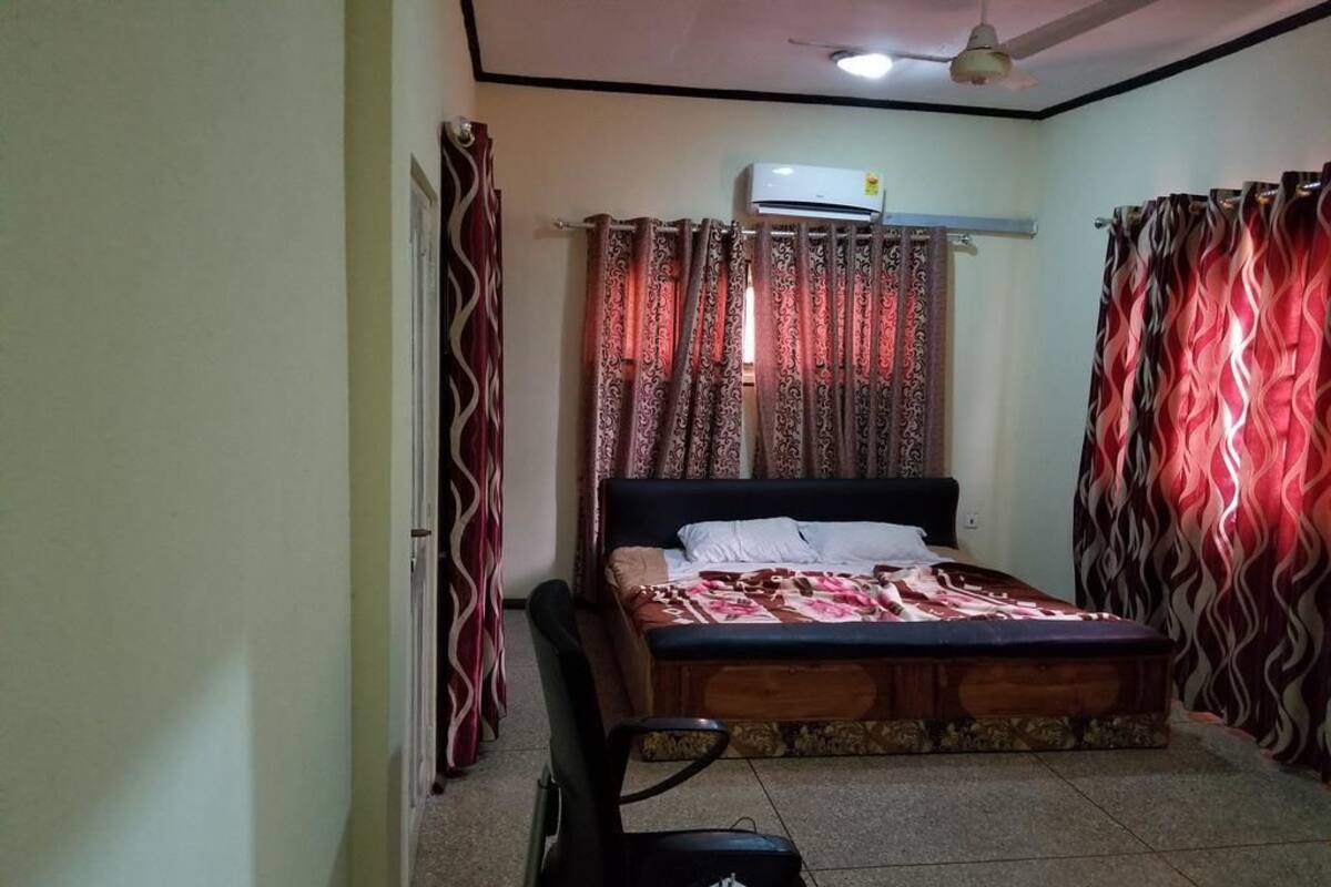 A bedroom with a bed, curtains, an air conditioning unit, and a ceiling fan.