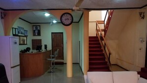 A hotel lobby with a reception desk, a clock, a staircase, and a white sofa. - Nass Lodge (Sunyani)