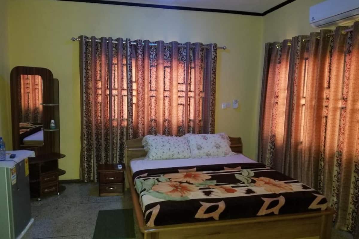 A bedroom with a bed, curtains, a mirror, a desk, and an air conditioner.