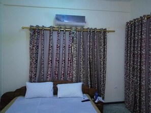 A hotel room with a bed, curtains, and an air conditioning unit. - Nass Lodge (Sunyani)