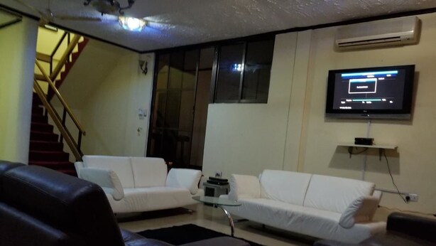 A living room with two white sofas, a dark brown leather armchair, a glass coffee table, and a flat-screen TV mounted on the wall. - Nass Lodge (Sunyani)