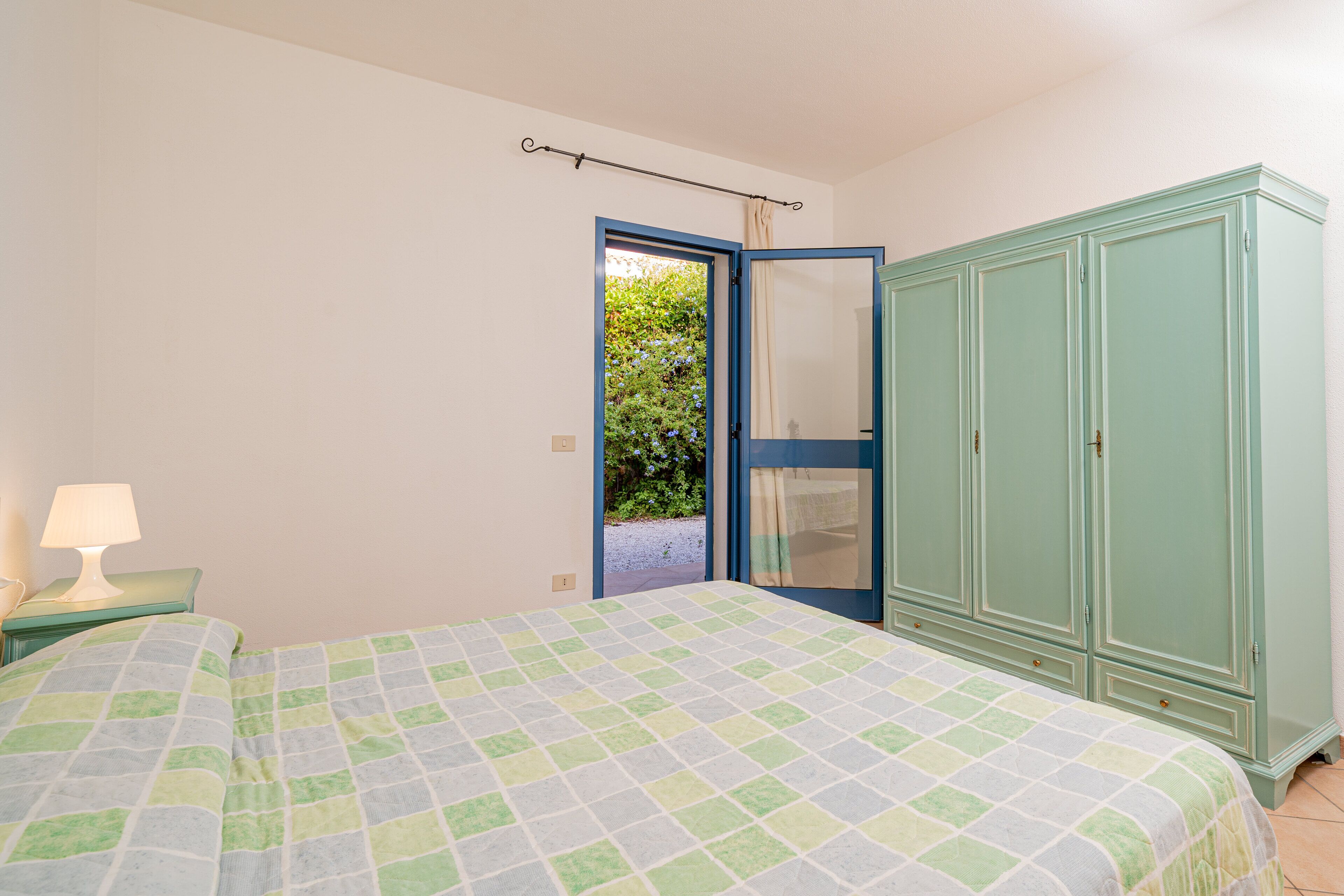 A bedroom with a bed, a nightstand, a wardrobe, and a door leading to a garden.