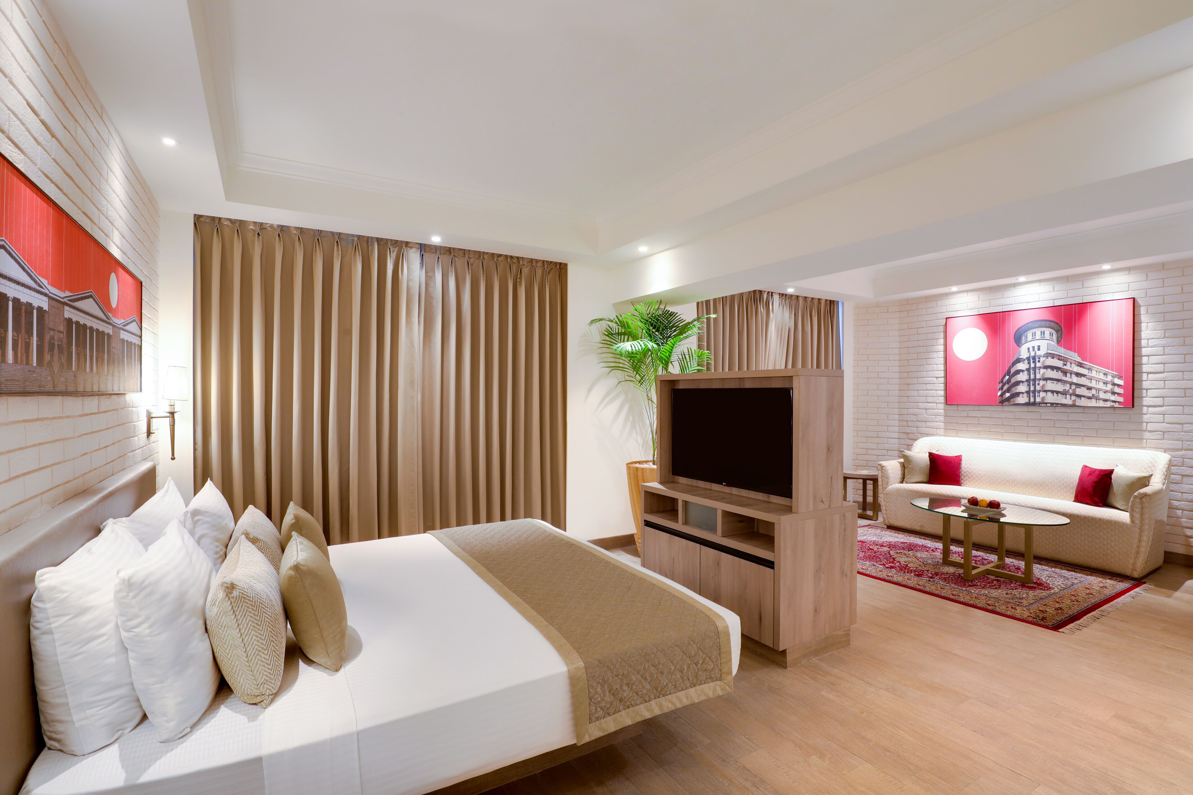 A modern hotel room with a large bed, a TV, a sofa, and a red accent wall.