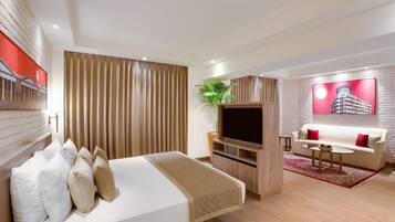 A modern hotel room with a large bed, a TV, a sofa, and a red accent wall.