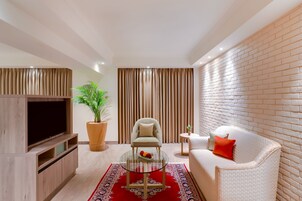A modern living room with a flat-screen TV, a glass coffee table, a sofa, a chair, and a potted plant.