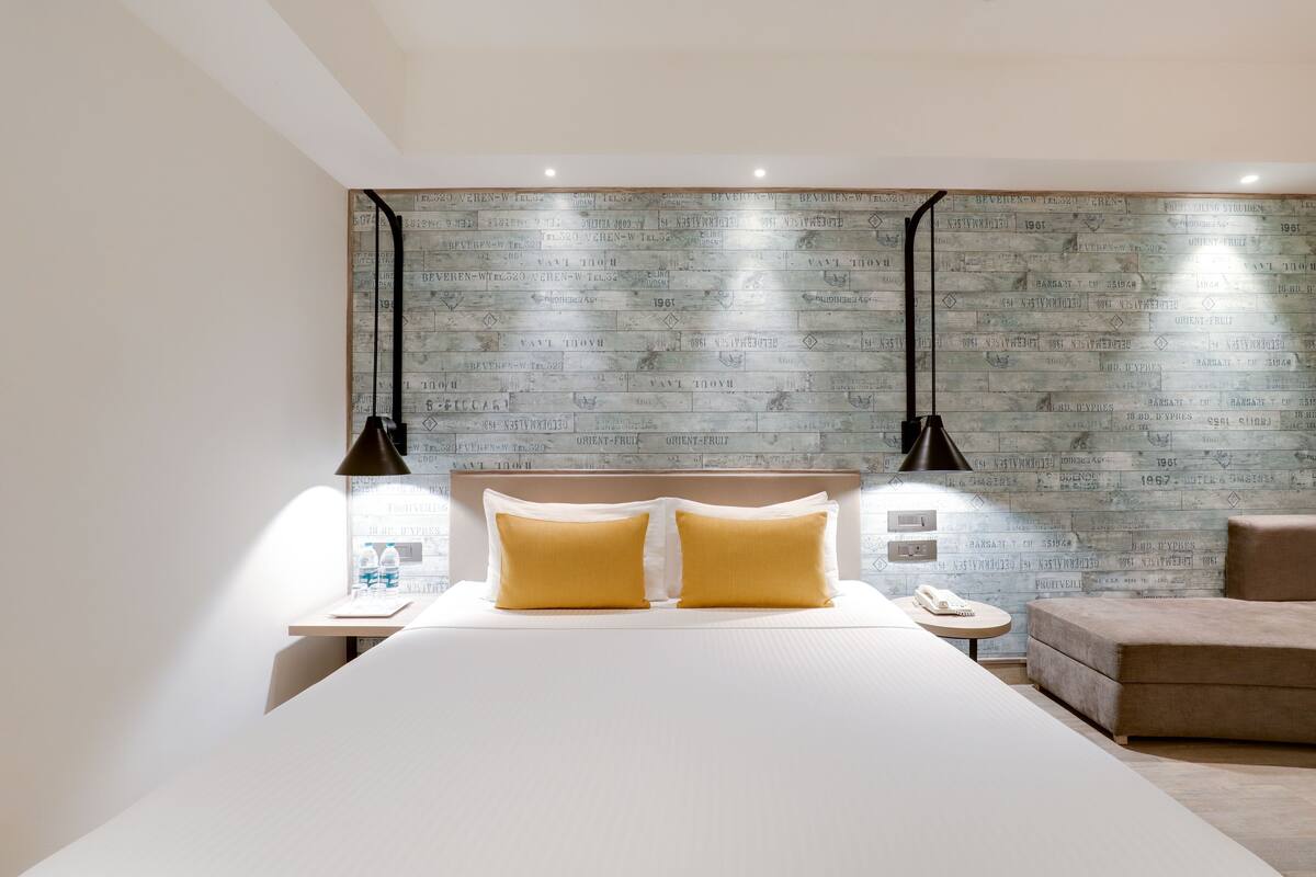 Une chambre d’hôtel moderne avec un grand lit, deux lampes de chevet, une petite table ronde et un canapé.