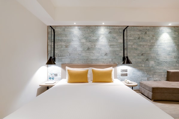 Ein modernes Hotelzimmer mit einem großen Bett, zwei Nachttischlampen, einem kleinen runden Tisch und einer Sitzecke.