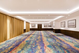 A spacious hotel room with a large, colorful carpet, a wooden panel wall, and framed pictures on the wall.