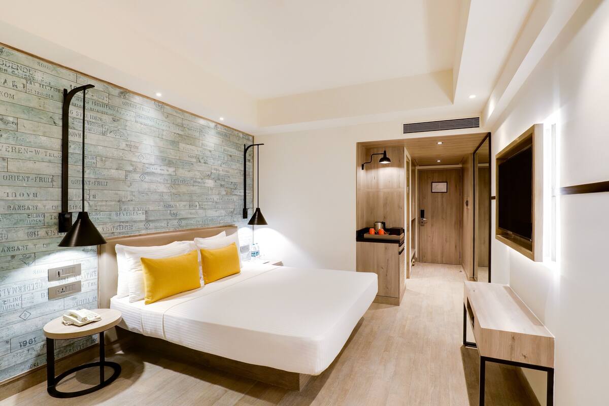 Une chambre d’hôtel moderne avec un grand lit, une petite table de chevet, un téléviseur fixé au mur et une armoire en bois.