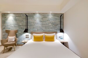 A modern hotel room with a large bed, two bedside lamps, a chair, and a wall with vintage-style wallpaper.