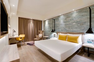 Habitación de hotel con una cama grande, un escritorio con silla, una mesita y una pared con diseño.