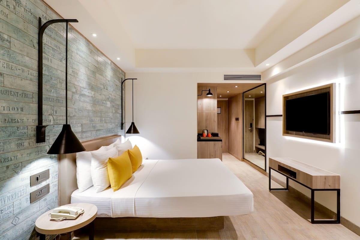 Une chambre d’hôtel moderne dotée d’un grand lit, d’une table de chevet, d’un téléviseur fixé au mur et d’un mur décoratif en bois orné de motifs textuels.