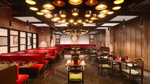 A restaurant with red booths and tables, multiple hanging lights, and a large mural on the back wall. - Lemon Tree Premier Mumbai Intl. Airport (Mumbai)