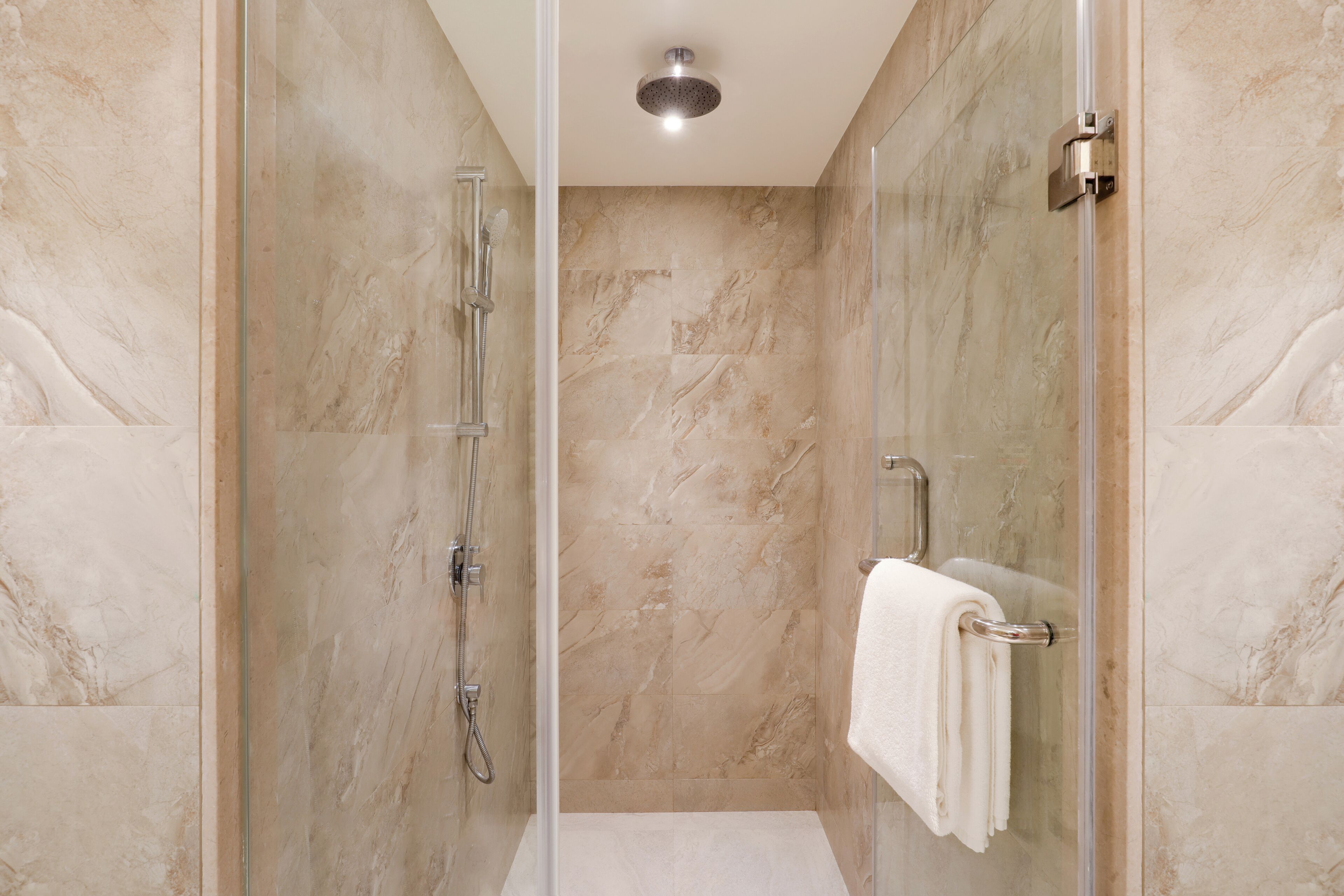 A modern bathroom with a glass-enclosed shower, marble walls, and a visible towel rack.