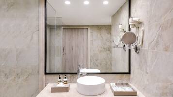 A modern bathroom with a large mirror, a round sink, and a hairdryer mounted on the wall.