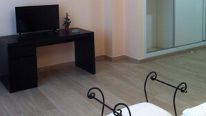 Une pièce avec un bureau noir, un téléviseur, une petite plante en pot, une chaise en métal et une porte-fenêtre coulissante donnant sur un placard.