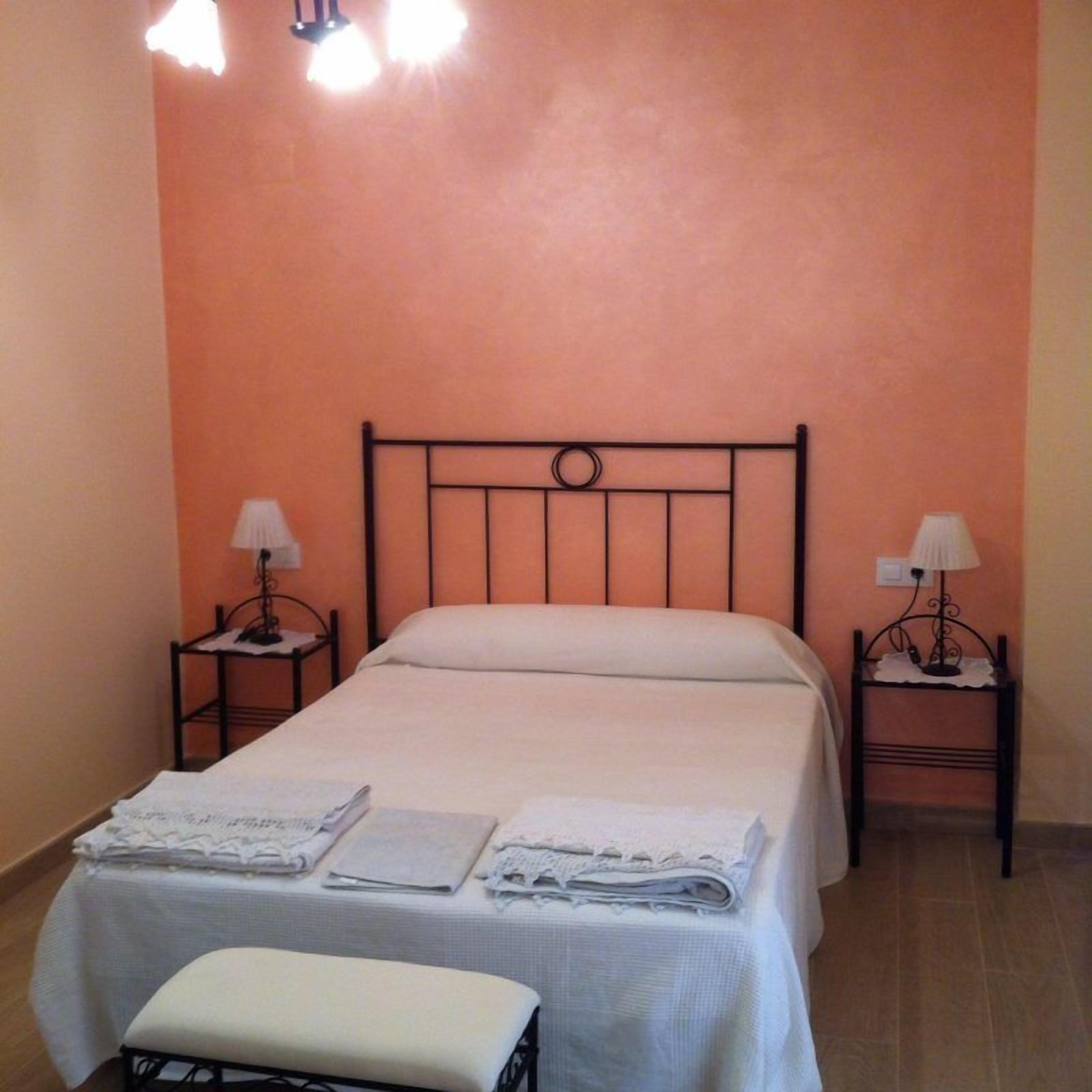 A single bed with a metal frame, two bedside tables with lamps, and a bench at the foot of the bed.