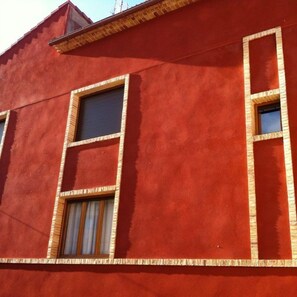 A red building with three windows, each with a wooden frame and a shutter. - Hostal Rural Sara (Villafeliche)