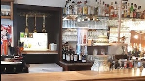 Een bar met houten krukken, een toog en planken vol flessen.
