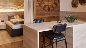 A modern room with a wooden accent wall, a large clock, a bed with a view, and a dining area with a bar stool and a plant.