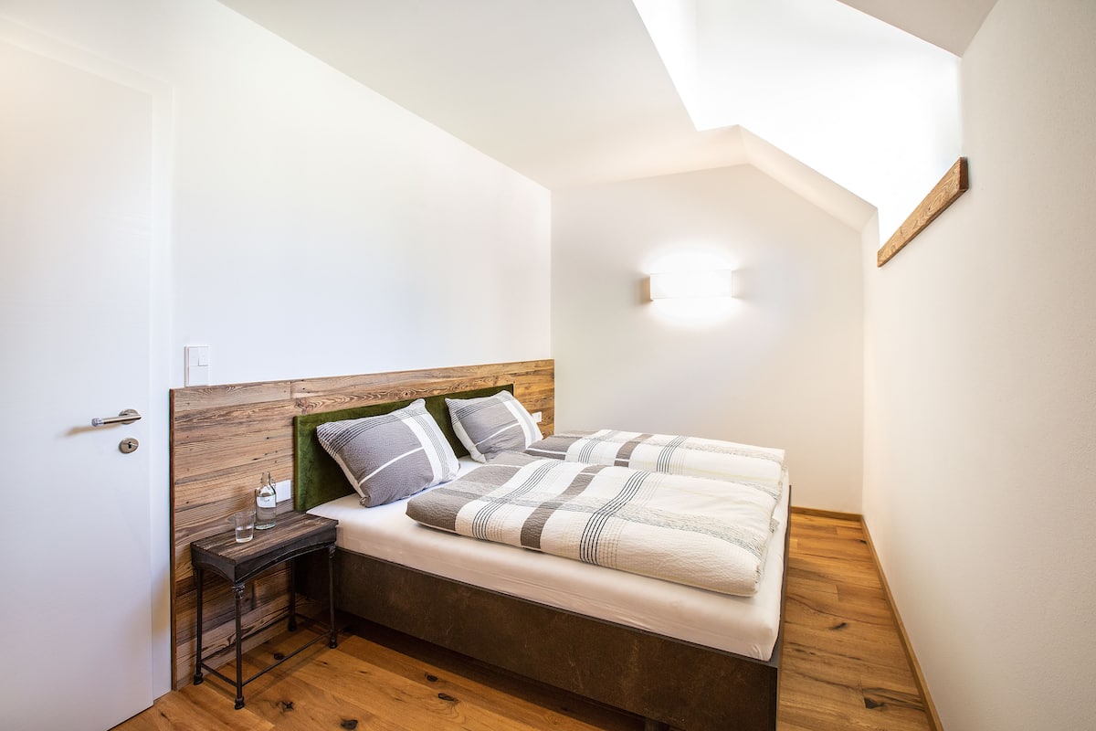 A bedroom with a wooden headboard, a bedside table with a bottle and glasses, and a bed with striped bedding.