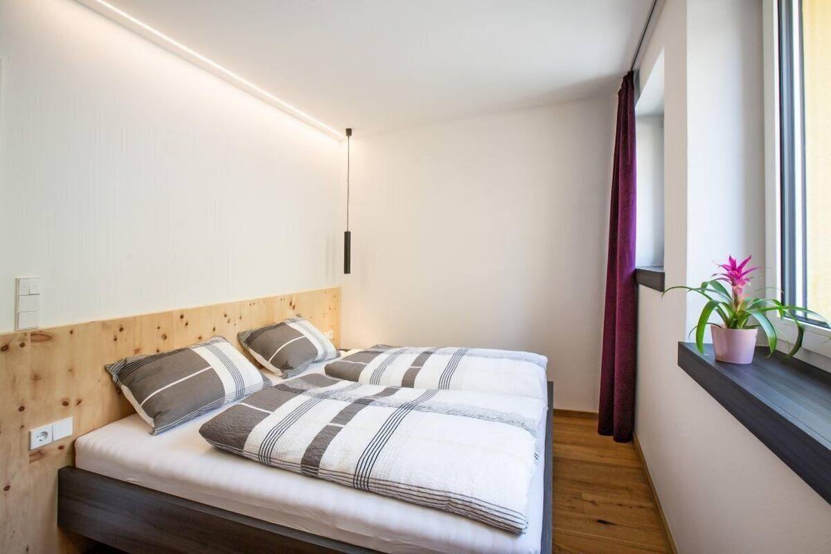 A bedroom with a wooden headboard, a bed with striped bedding, a bedside table, a potted plant, and a window with curtains.