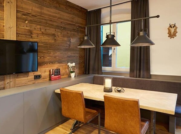 A modern kitchen with wooden accents, a built-in TV, pendant lights, and a window with curtains.