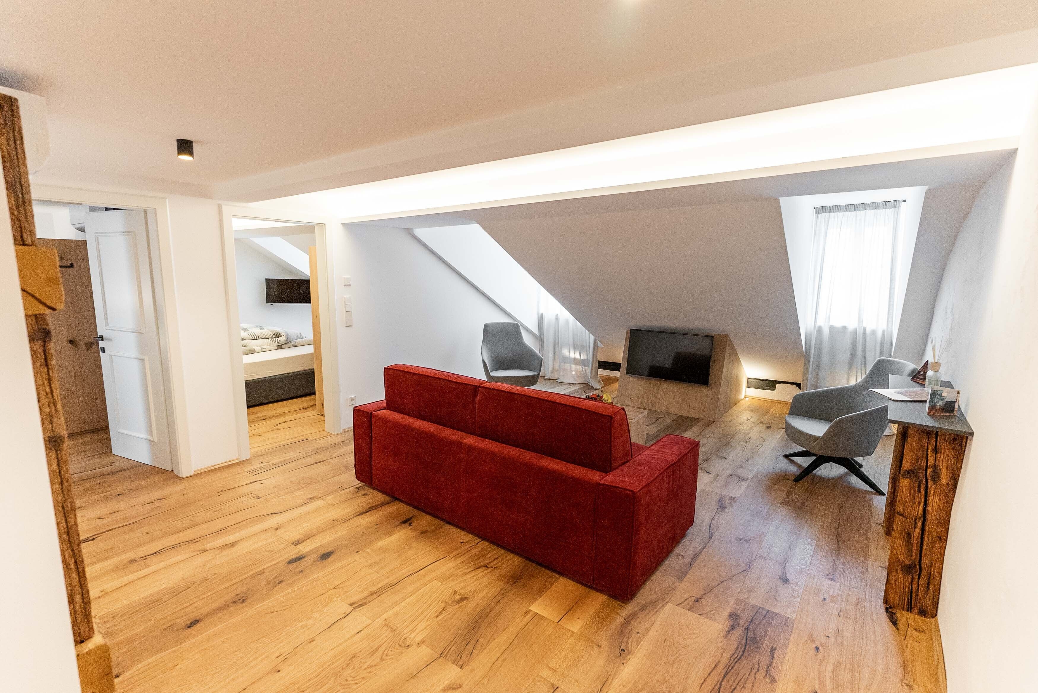 A spacious loft with a red sofa, wooden flooring, and a dining area with a wooden table and chairs.