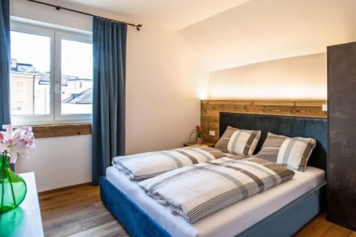 A bedroom with a bed, a wardrobe, a window with curtains, and a vase with flowers.
