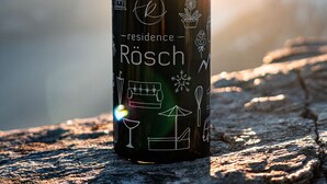 A water bottle with various icons and the text "Residence Rosch" on a textured surface with a blurred background.