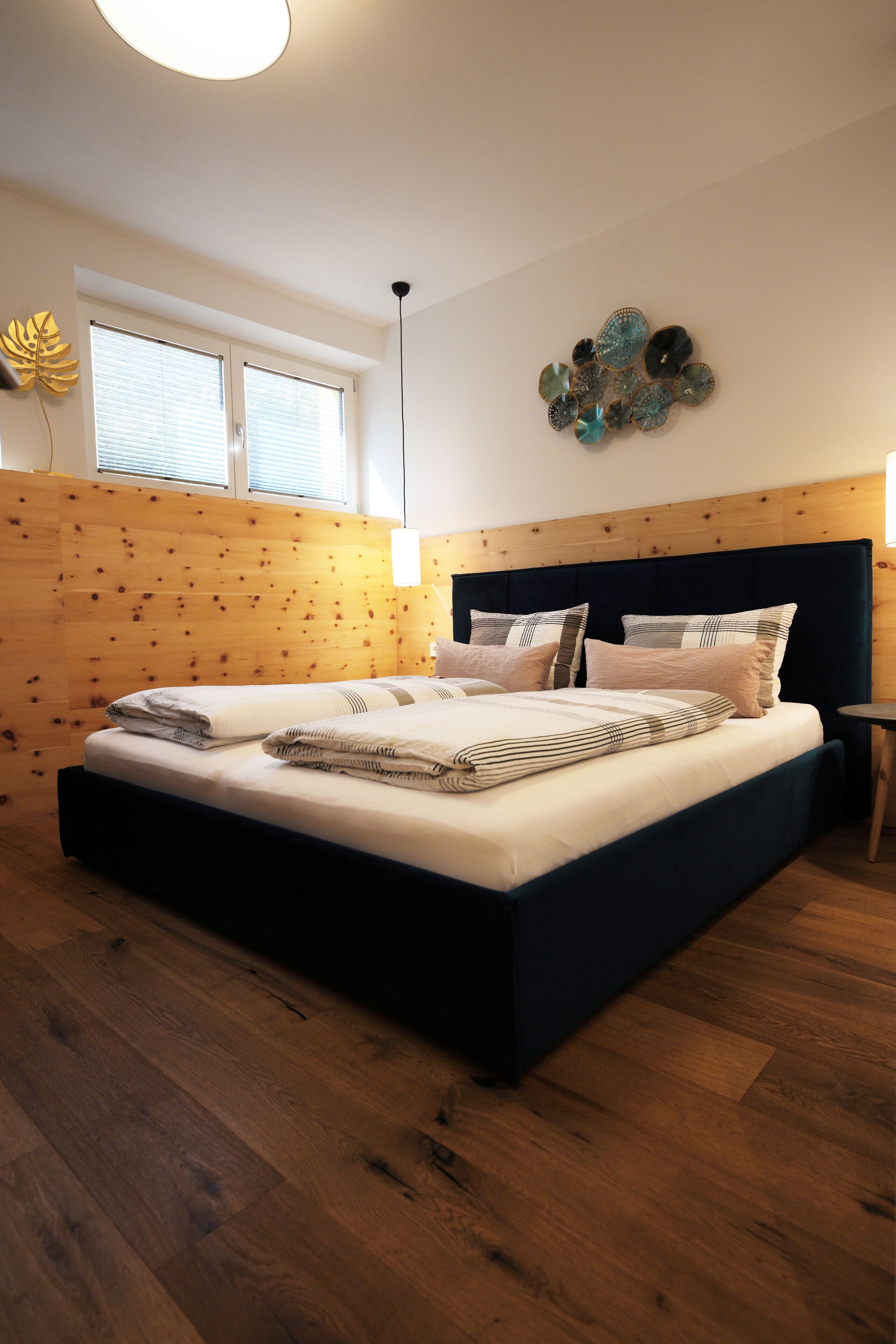 A bedroom with a large bed, wooden paneling on the walls, a window with blinds, and a decorative wall piece.