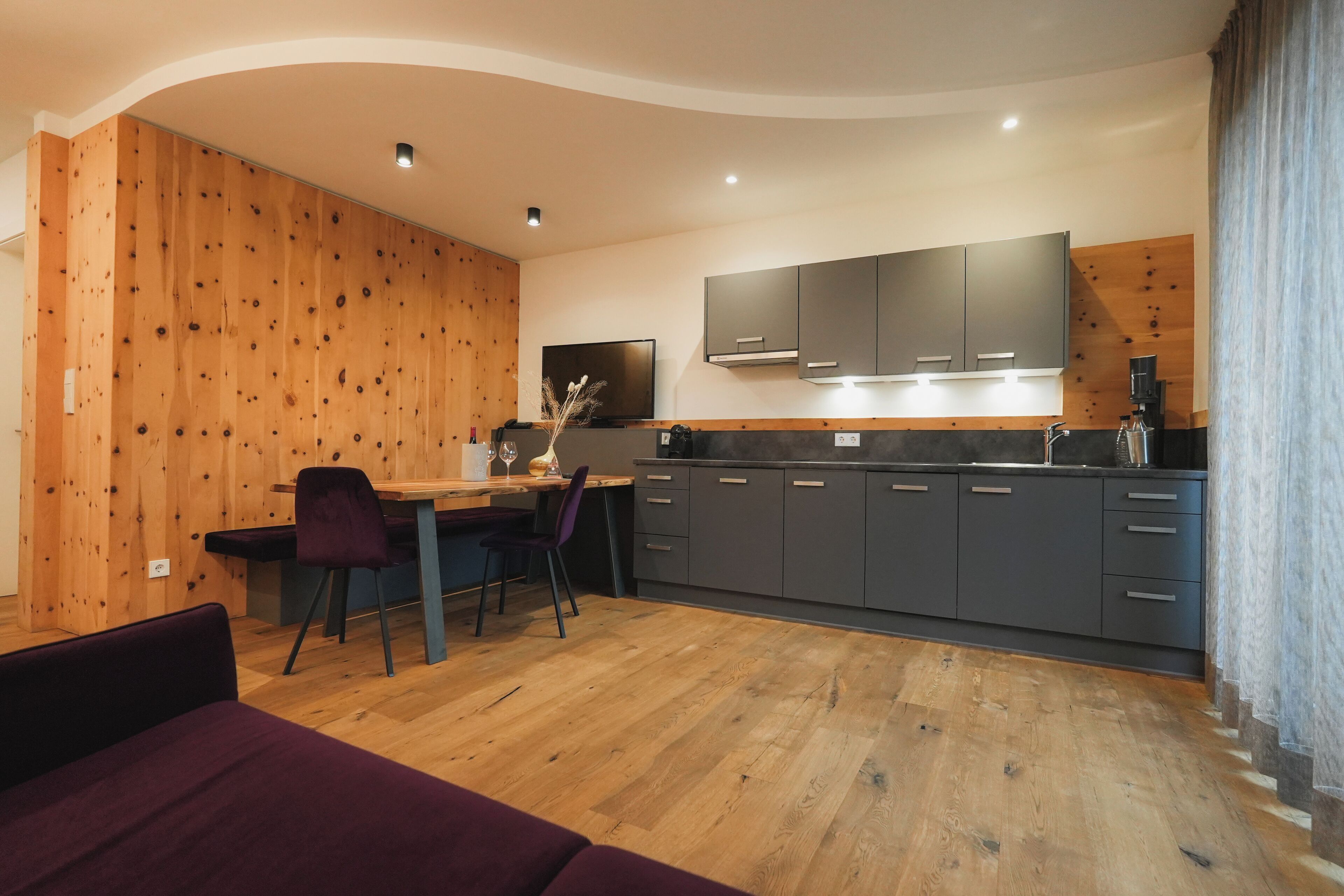 Une cuisine moderne agrémentée d’éléments en bois, un coin repas avec une table et des chaises, et un téléviseur encastré.