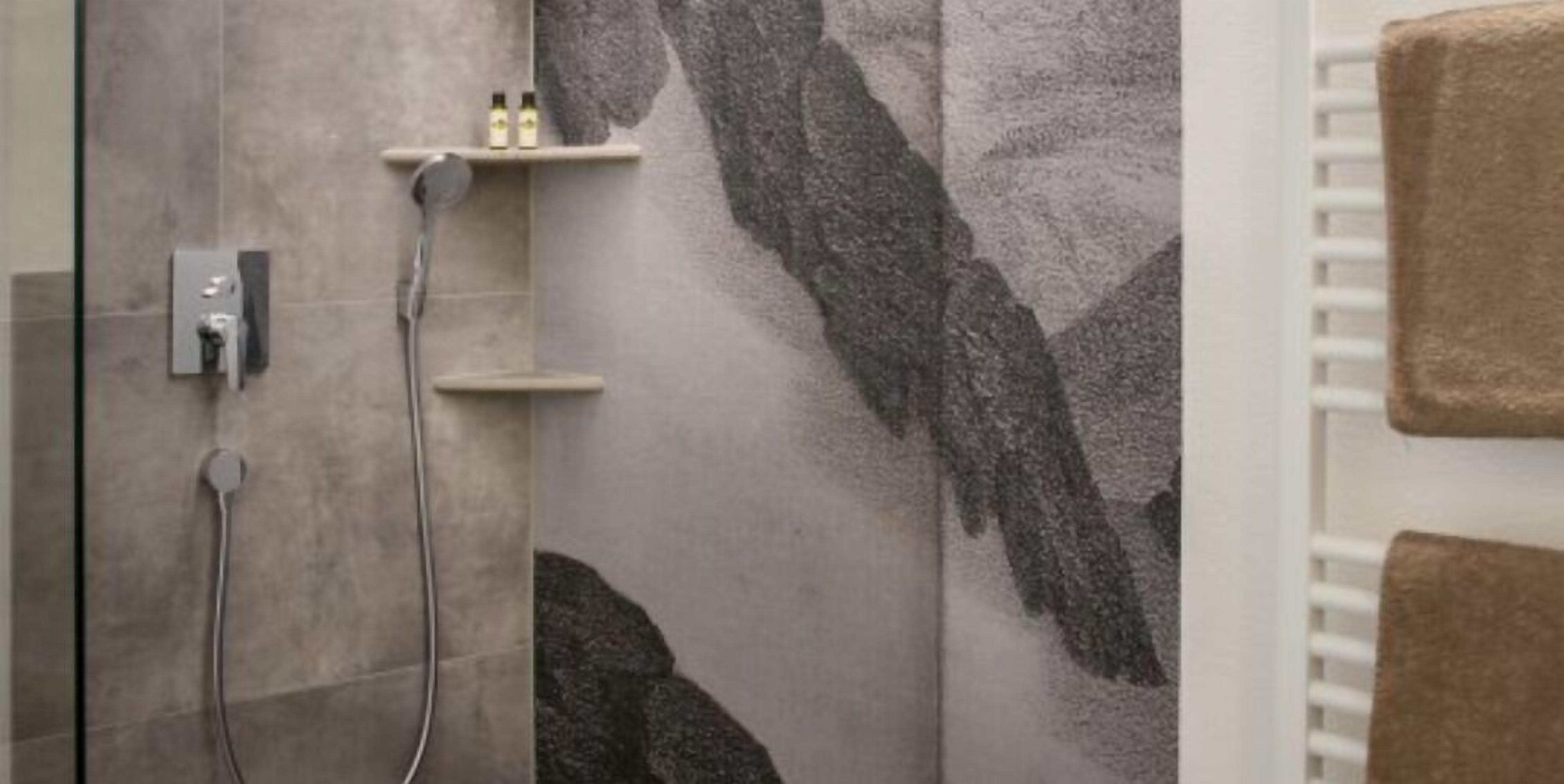 A shower area with a wall-mounted faucet and a handheld showerhead. There is a shelf with toiletries.