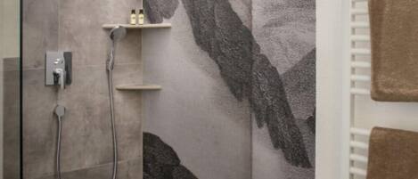 A shower area with a wall-mounted faucet and a handheld showerhead. There is a shelf with toiletries.