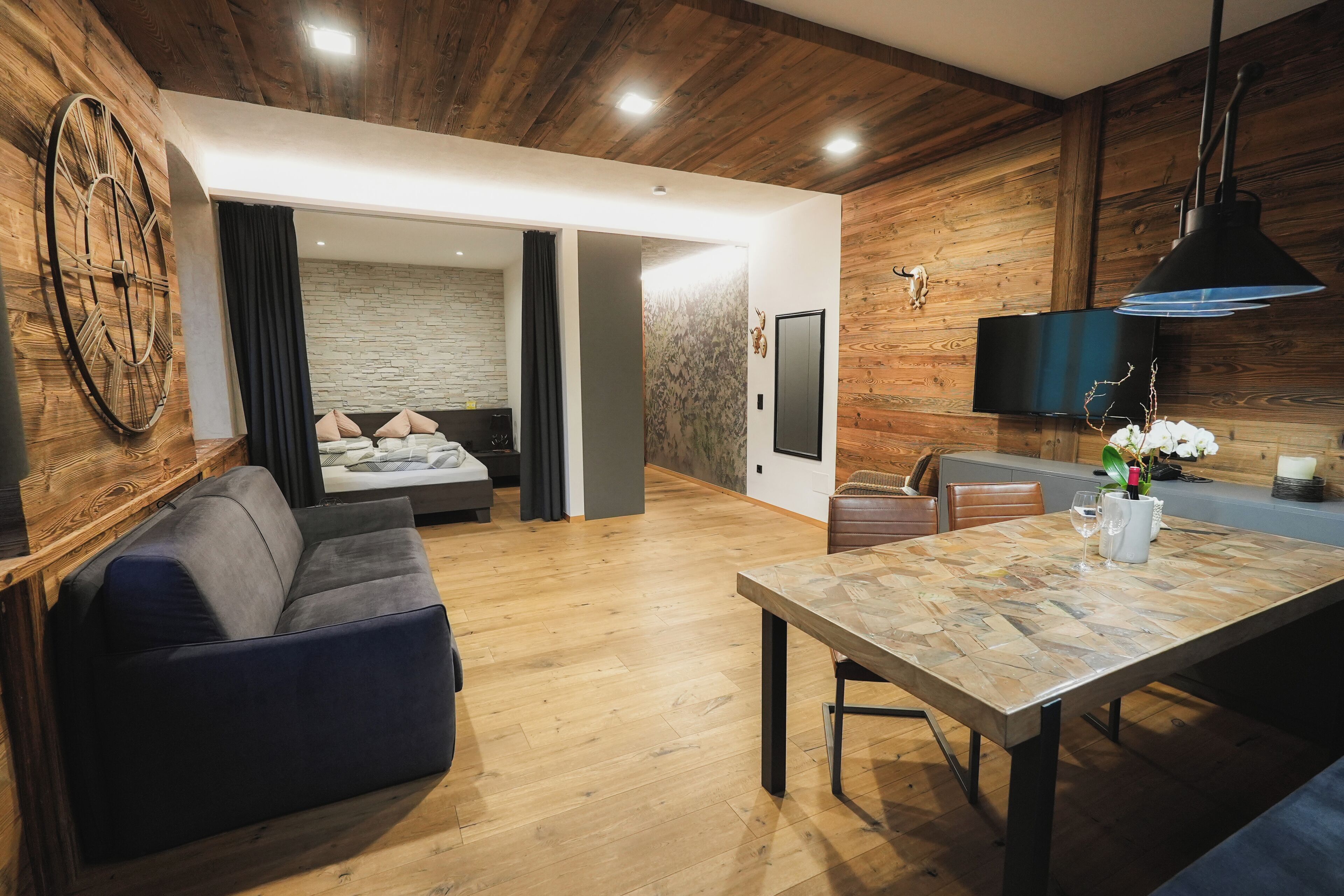 A modern living room with a sofa, a dining table, and a kitchen area with a TV and wooden walls.