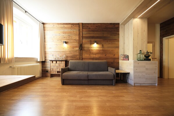 A modern living room with a wooden floor, a grey sofa, and a wooden accent wall. - Residence Rösch (Merano)