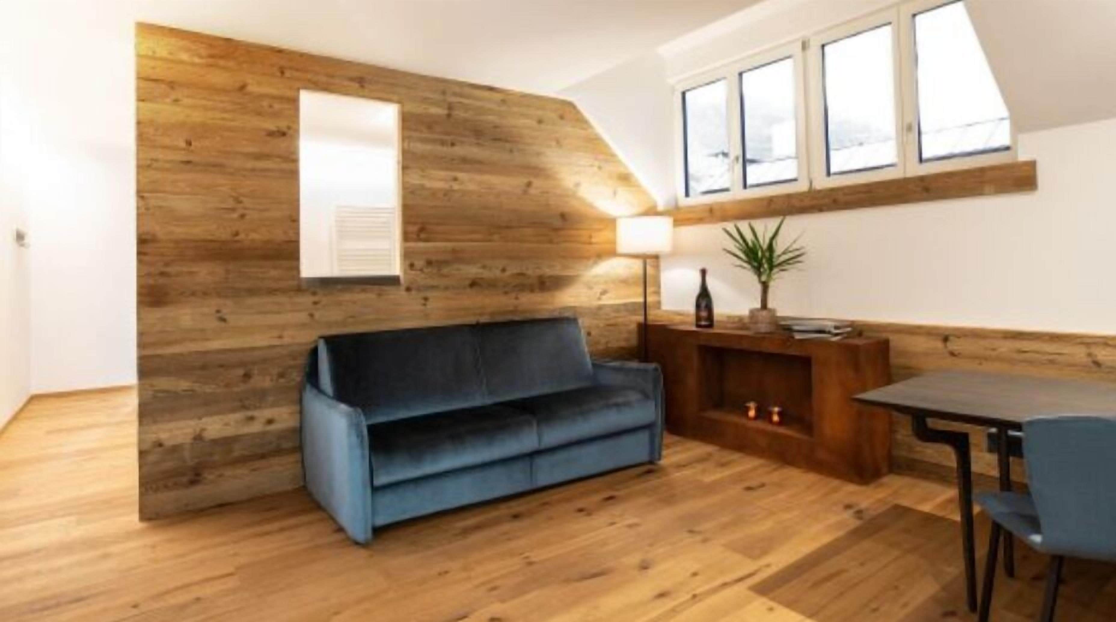 A cozy living area with a wooden accent wall, a blue sofa, a wooden coffee table, and a dining table with chairs.