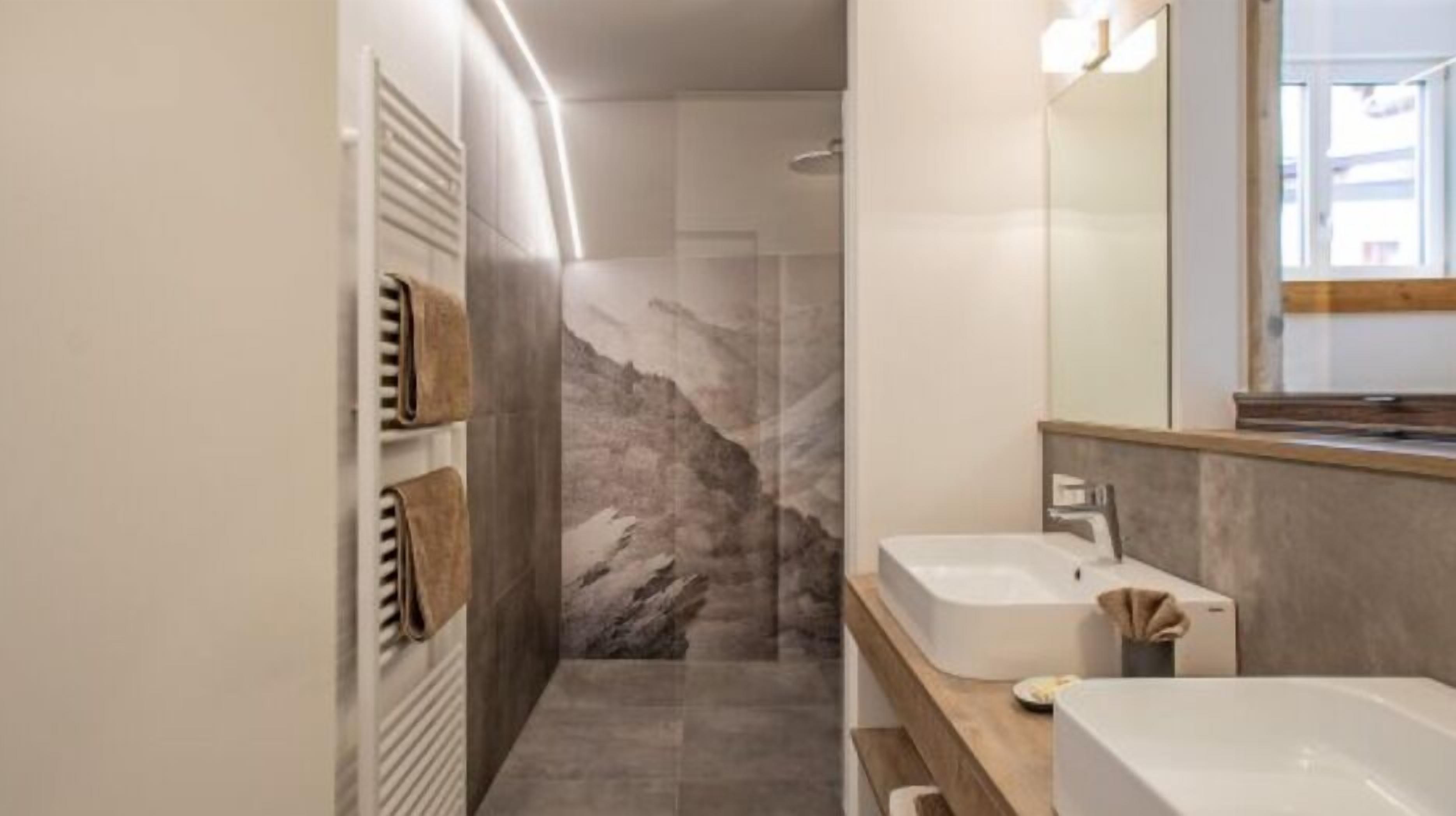 A modern bathroom with a marble shower wall, two sinks, and a large mirror.