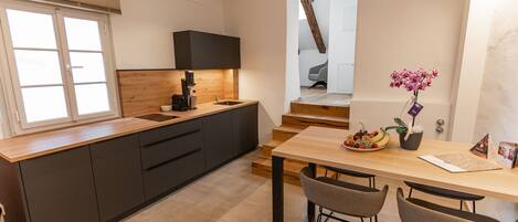 A modern kitchen with dark cabinets, a wooden countertop, and a built-in stove. There is a dining area with a wooden table and bar stools.